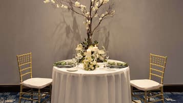 A round table with a white tablecloth, two chairs, a floral centerpiece, and a lit candle.