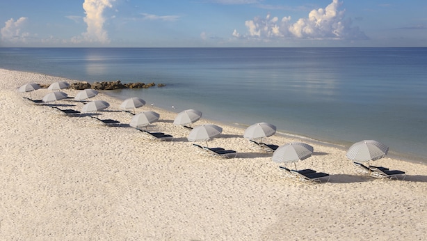 A beach with white sand, clear blue water, and striped umbrellas. - Edgewater Beach Hotel (Naples)