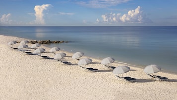 Een privéstrand, wit zand, ligstoelen aan het strand, parasols