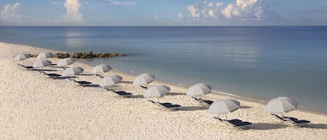 Een privéstrand, wit zand, ligstoelen aan het strand, parasols