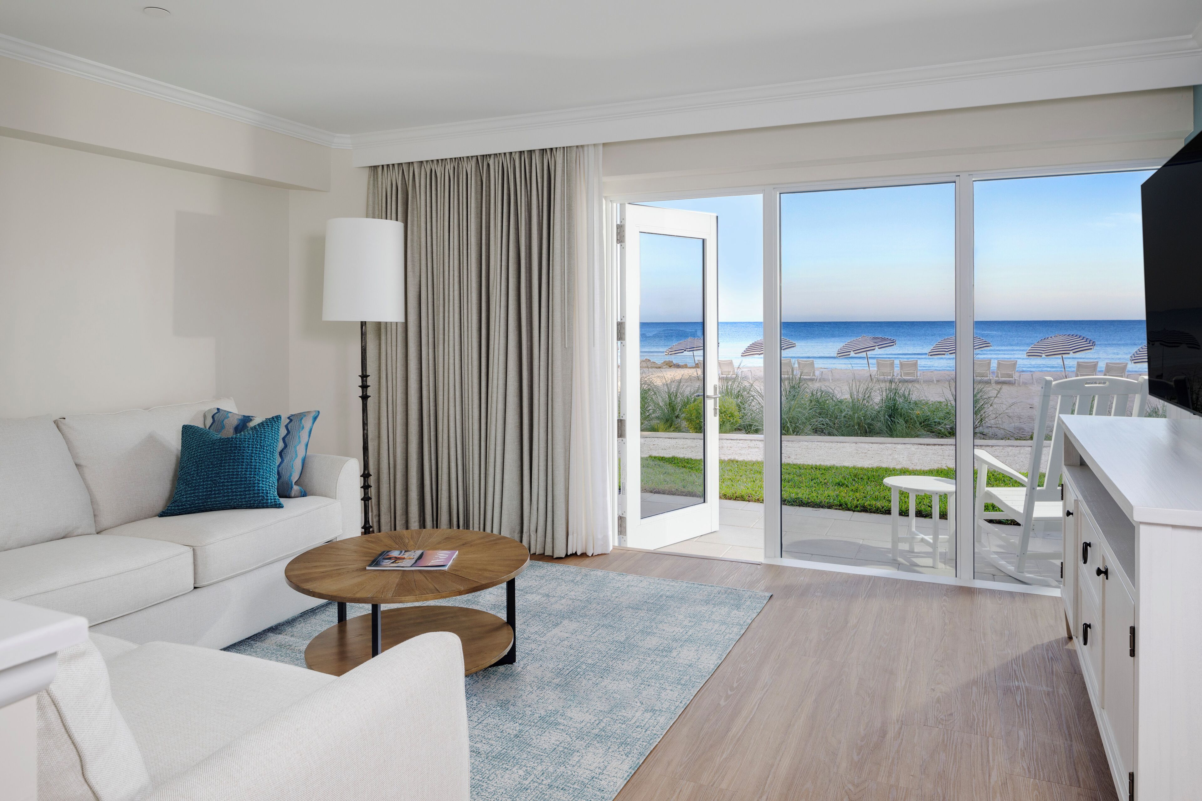 A modern hotel room with a sofa, coffee table, and a view of the beach.