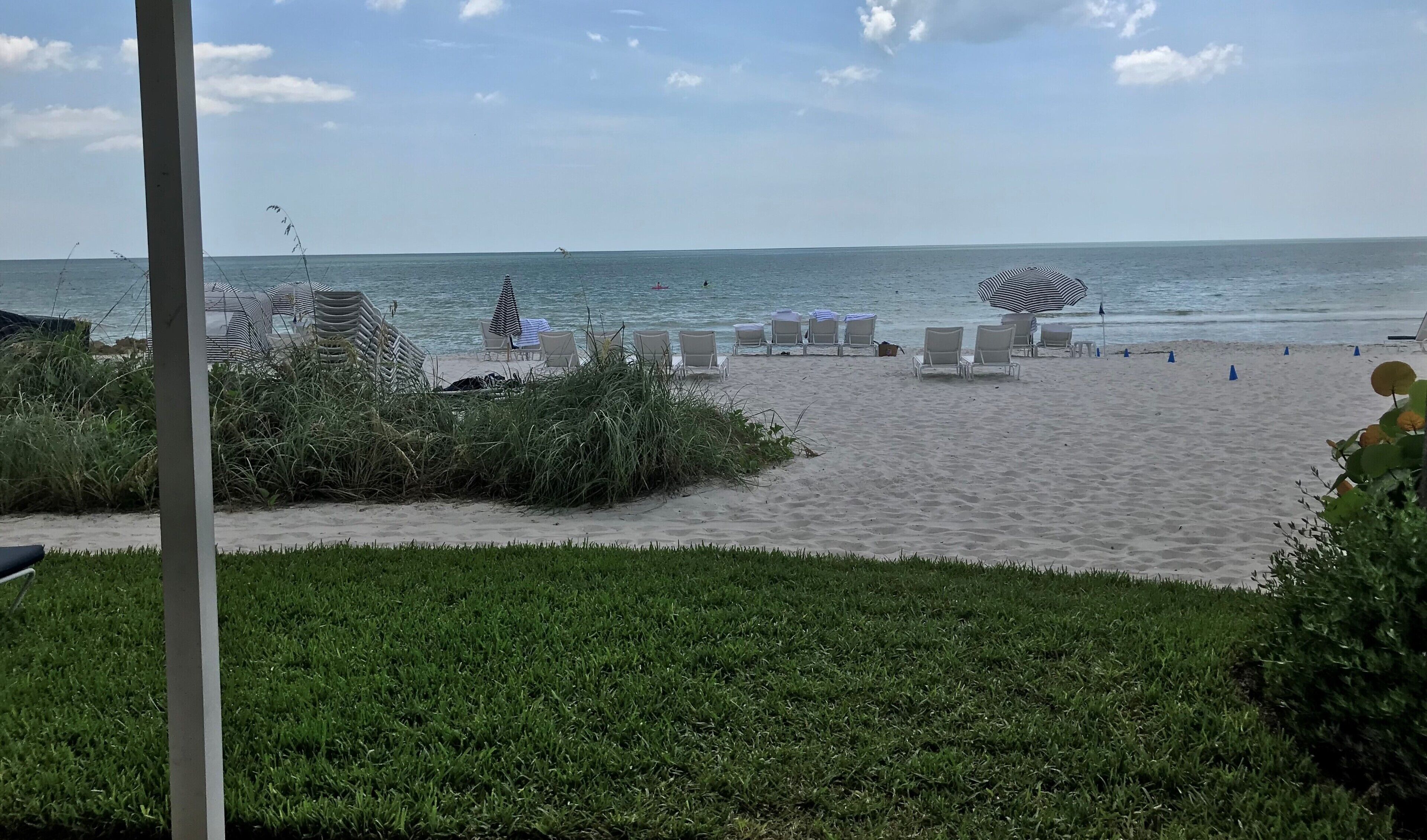 A beach with white lounge chairs, a striped umbrella, and a clear view of the sea.