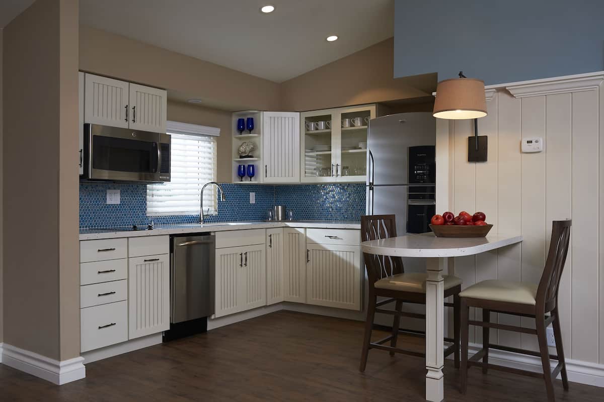A kitchen with white cabinets, a microwave, a refrigerator, and a dining table with chairs.