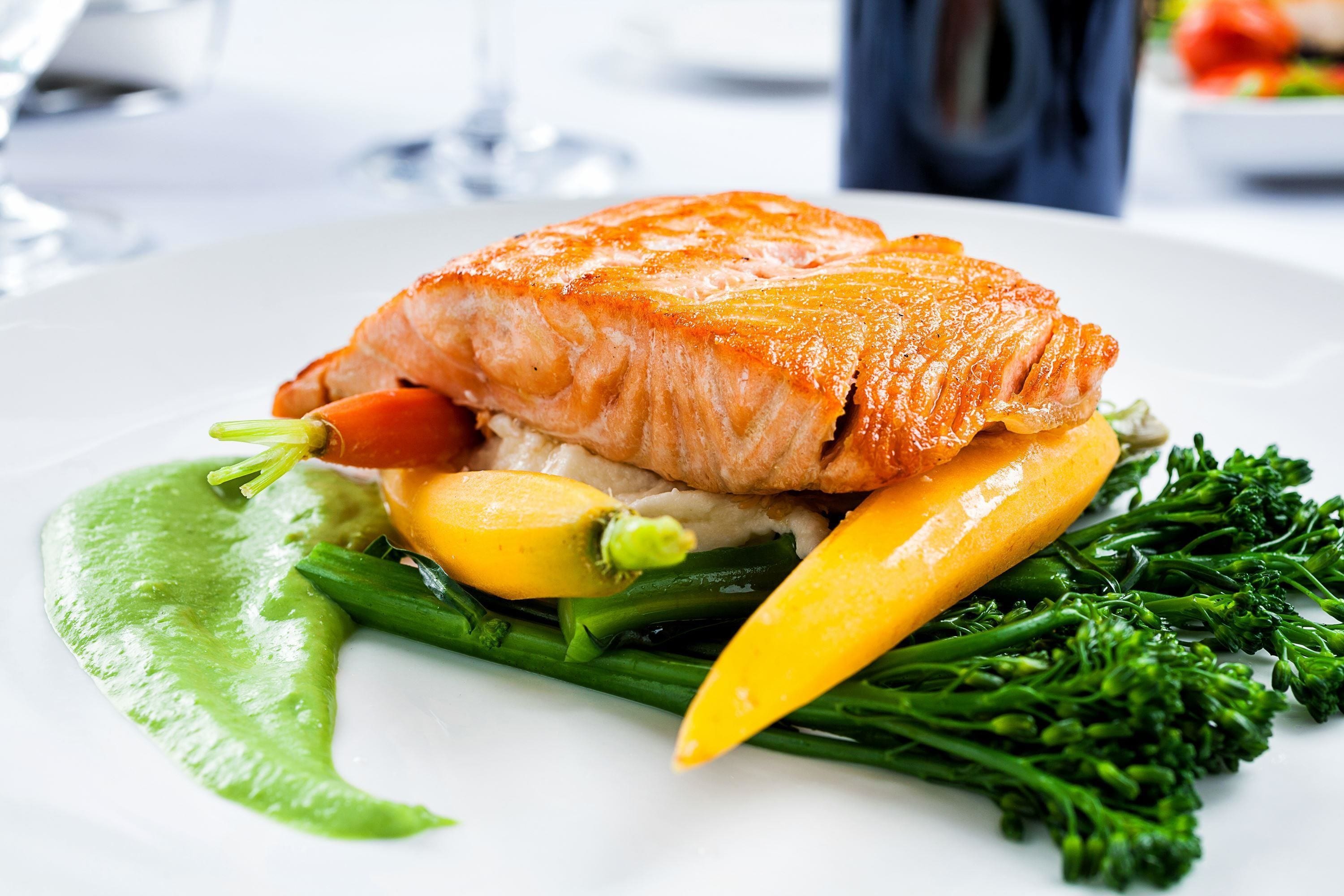 A plate of food with salmon, vegetables, and a green sauce.