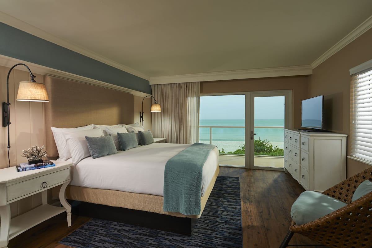 A bedroom with a bed, bedside lamps, a dresser, a television, and a view of the ocean.