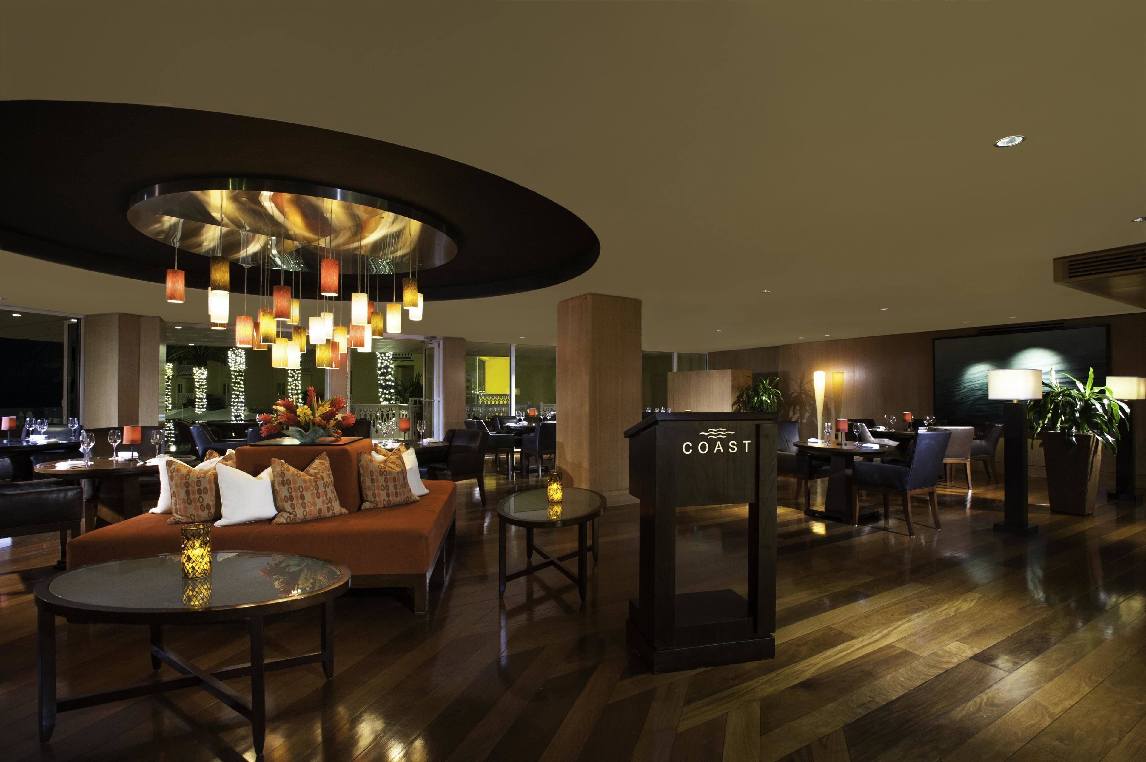 Un vestíbul modern amb una zona de seients circular, un bar i una recepció amb el nom 'COAST'.