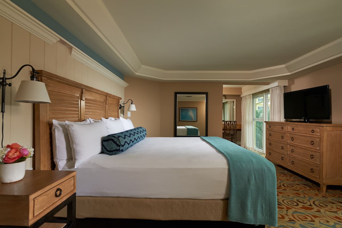 A hotel room with a large bed, wooden headboard, a dresser, a TV, and a window with curtains.