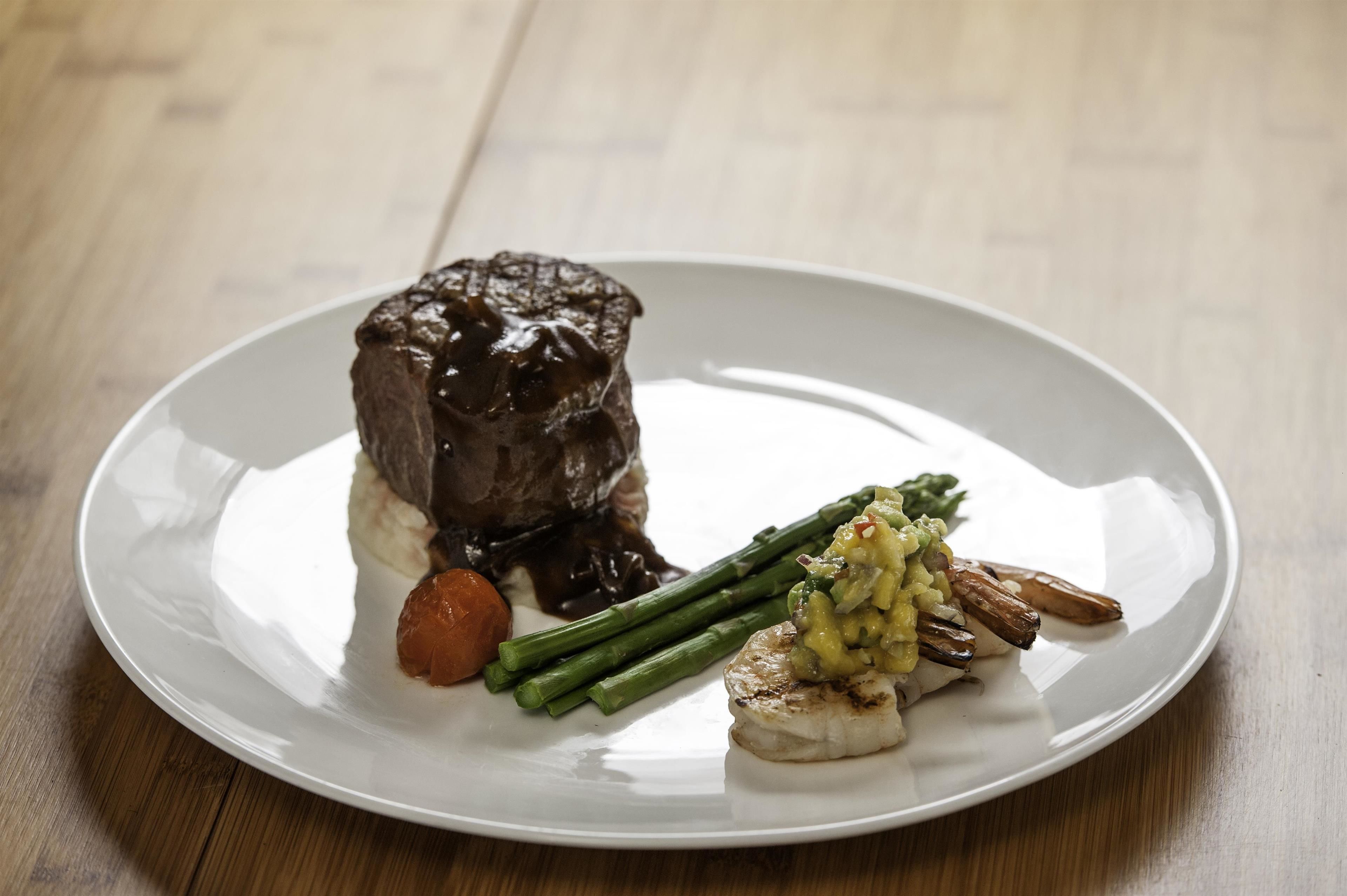 A plate with a piece of meat, asparagus, and a small orange.