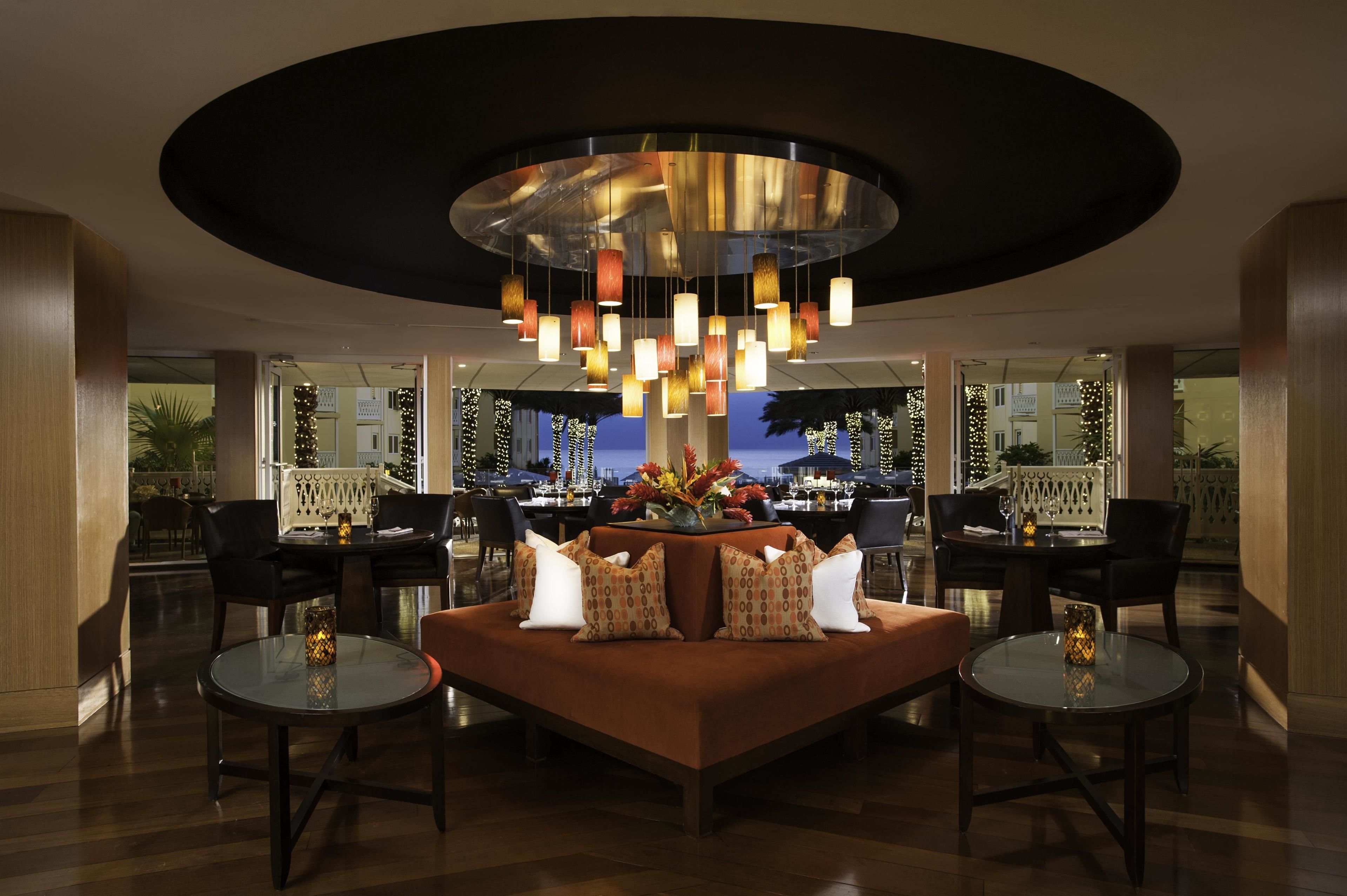 A modern lobby with a central seating area, a large chandelier, and a view of the outdoor dining area.