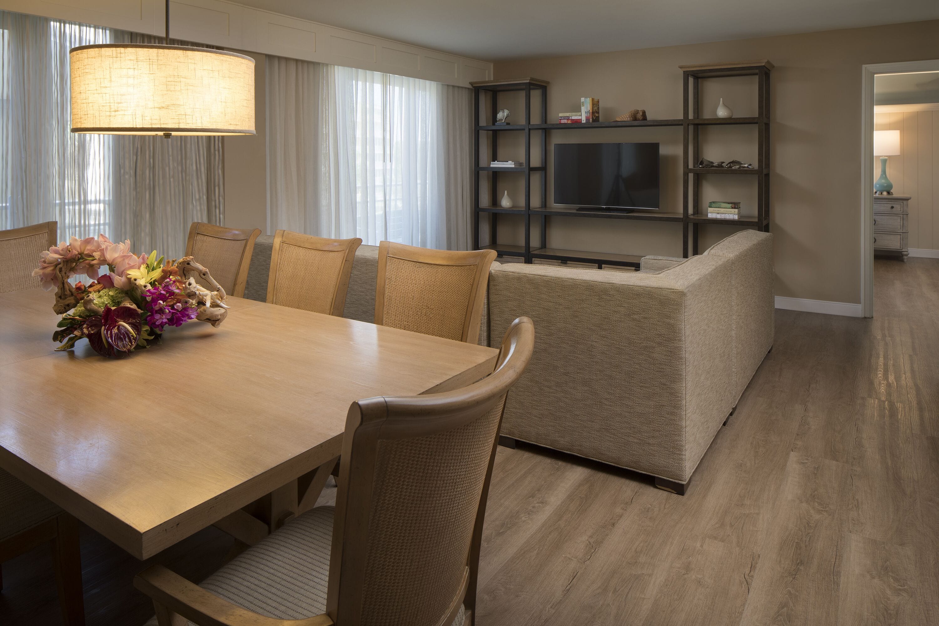 A modern hotel room with a dining area, a sofa, a TV, and a bookshelf.