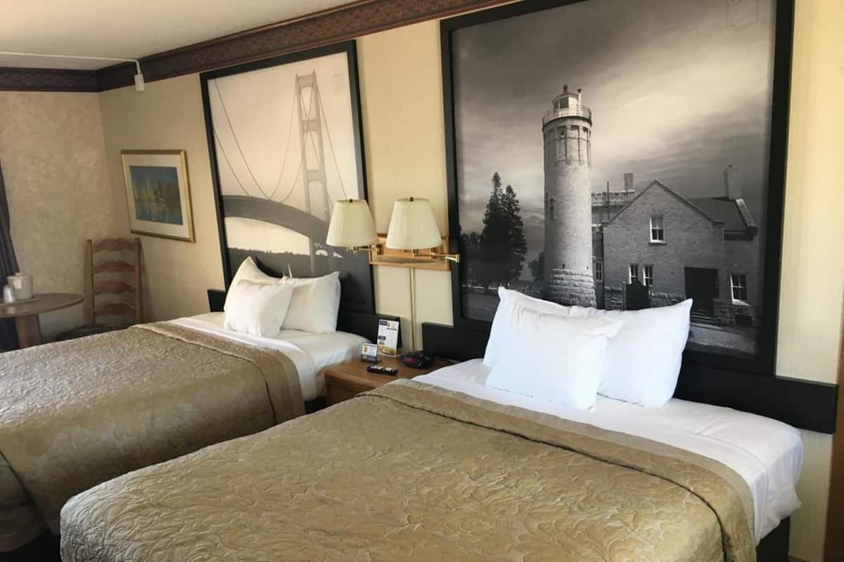Ein Hotelzimmer mit zwei Betten, einem Nachttisch, einer Lampe und einem gerahmten Bild eines Leuchtturms.