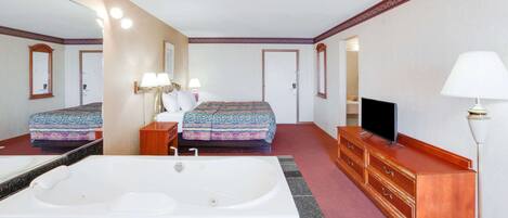 Una habitación de hotel con un espejo grande, una cama con ropa de cama estampada, un televisor, un aparador de madera y una bañera espaciosa.