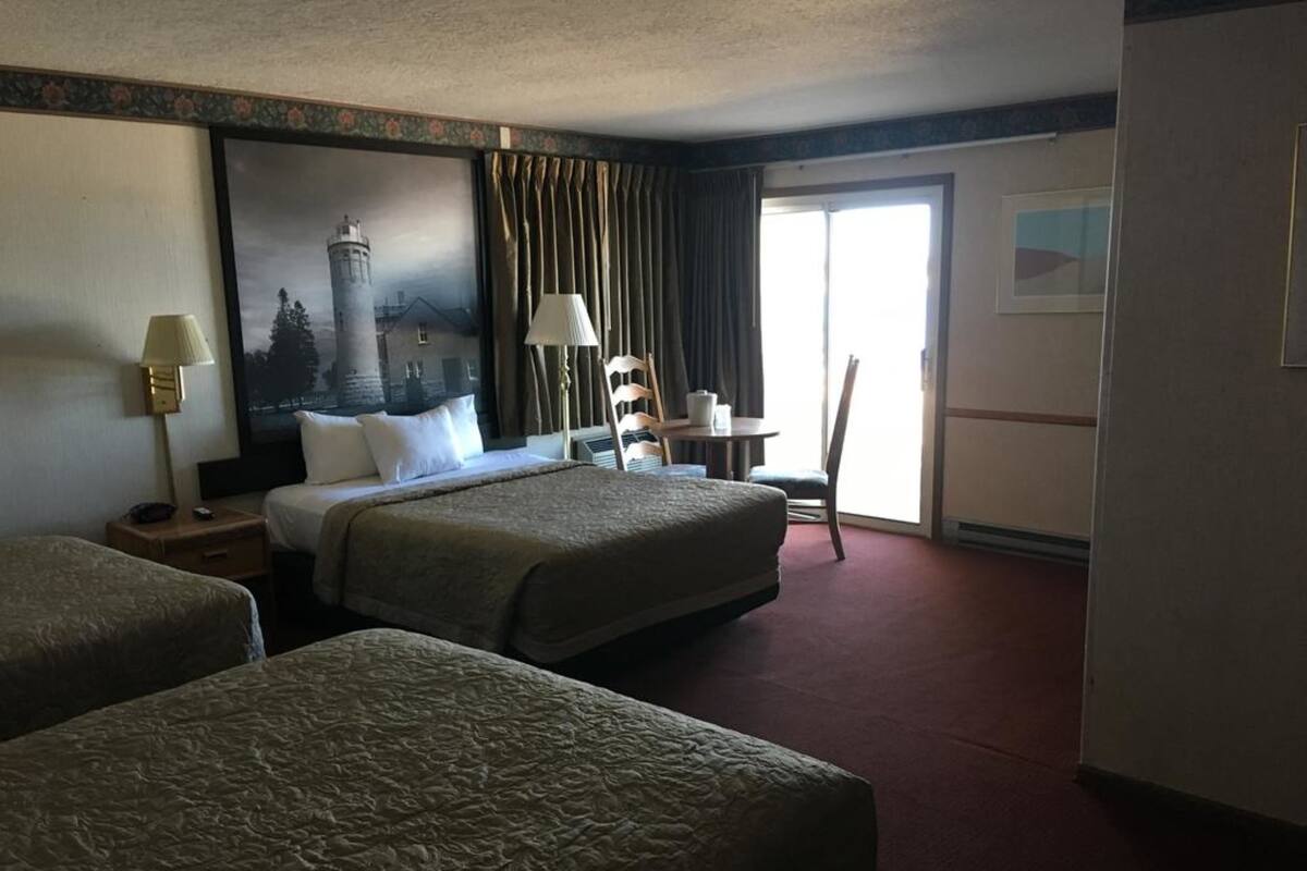 Ein Hotelzimmer mit zwei Betten, einem Schreibtisch, einem Sessel, einer Lampe und einem Bild an der Wand.