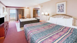 A hotel room with a large bed, a desk with a television, a bathroom with a bathtub, and a balcony with a view of the sea. - Super 8 by Wyndham Mackinaw City/Beachfront Area (Mackinaw City)