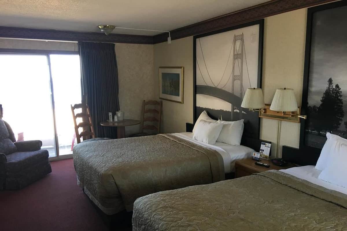 Ein Hotelzimmer mit zwei Betten, einem Schreibtisch, einem Stuhl und einem großen Fenster mit Blick auf eine Brücke.