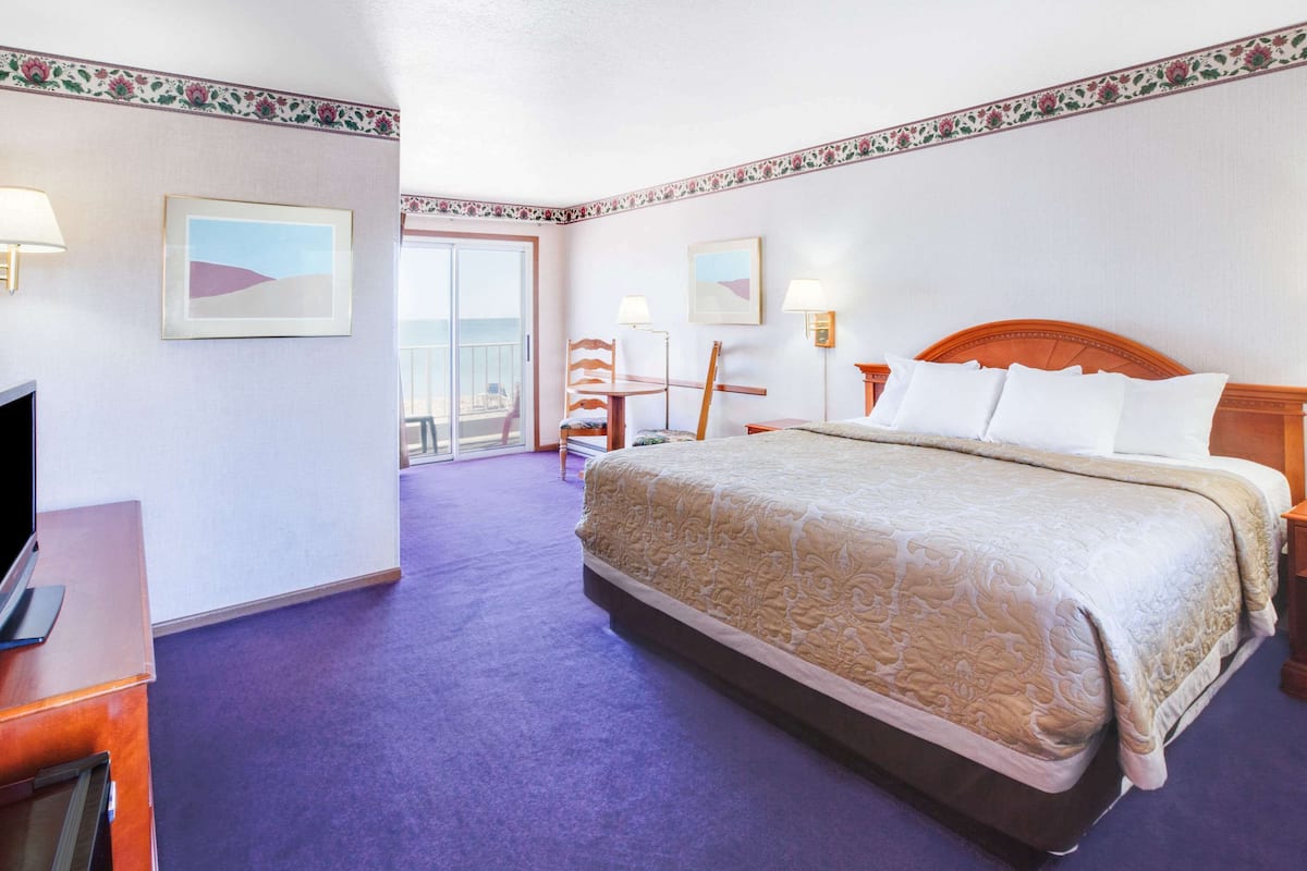 Ein Hotelzimmer mit einem großen Bett, einem Schreibtisch mit Computer, einem Stuhl und einem Balkon mit Blick.