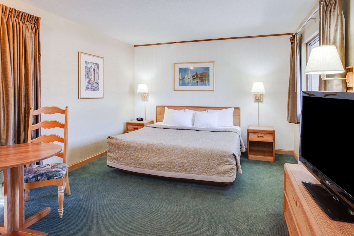 Ein Hotelzimmer mit einem großen Bett, zwei Nachttischen, einem Fernseher, einem Sessel und zwei Lampen.