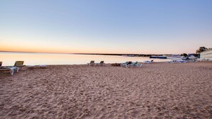 A beach with sun loungers and a boat docked on the shore. - Super 8 by Wyndham Mackinaw City/Beachfront Area (Mackinaw City)