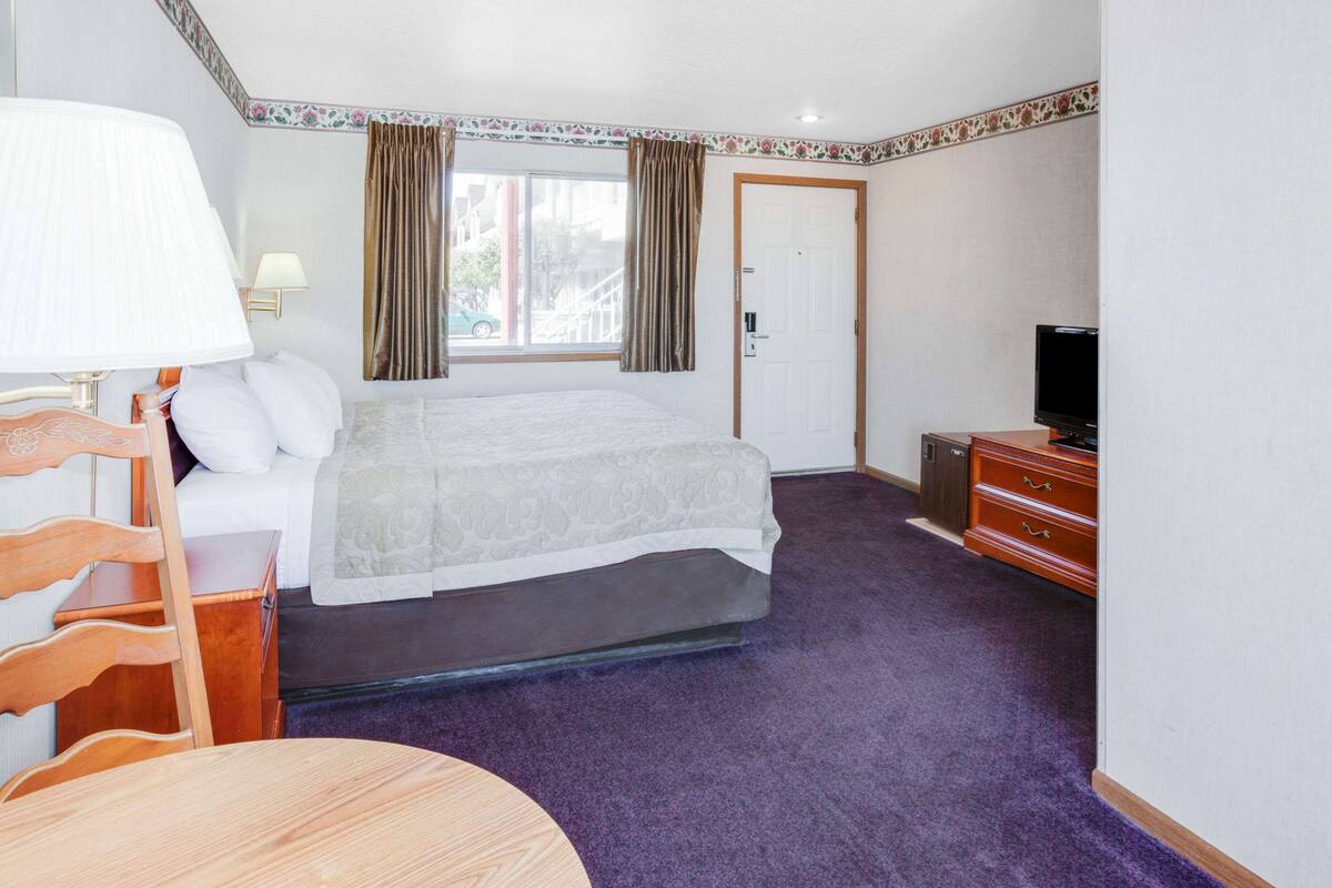 Ein Hotelzimmer mit Bett, Fernseher, Kommode, Stuhl und Schreibtisch.