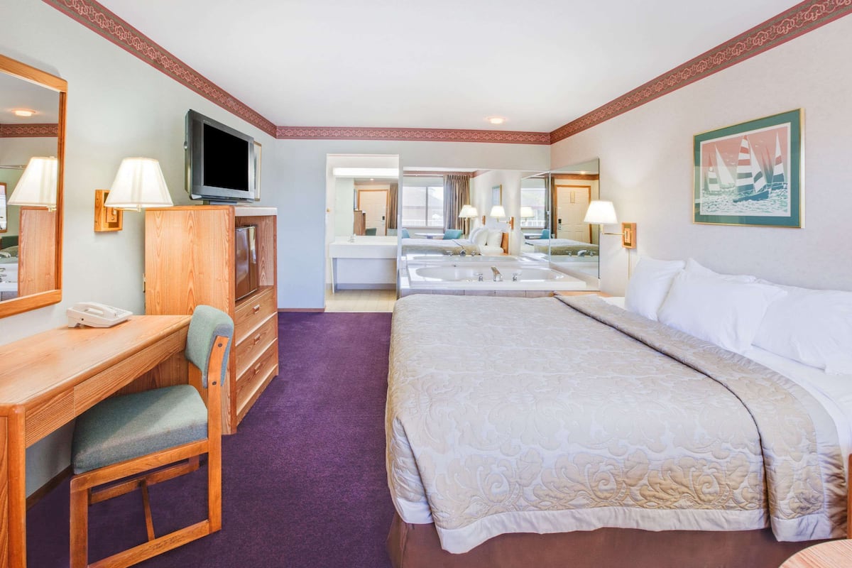 Ein Hotelzimmer mit einem großen Bett, einem Schreibtisch mit Stuhl, einem Fernseher und einem Badezimmer mit Spiegel und Waschbecken.