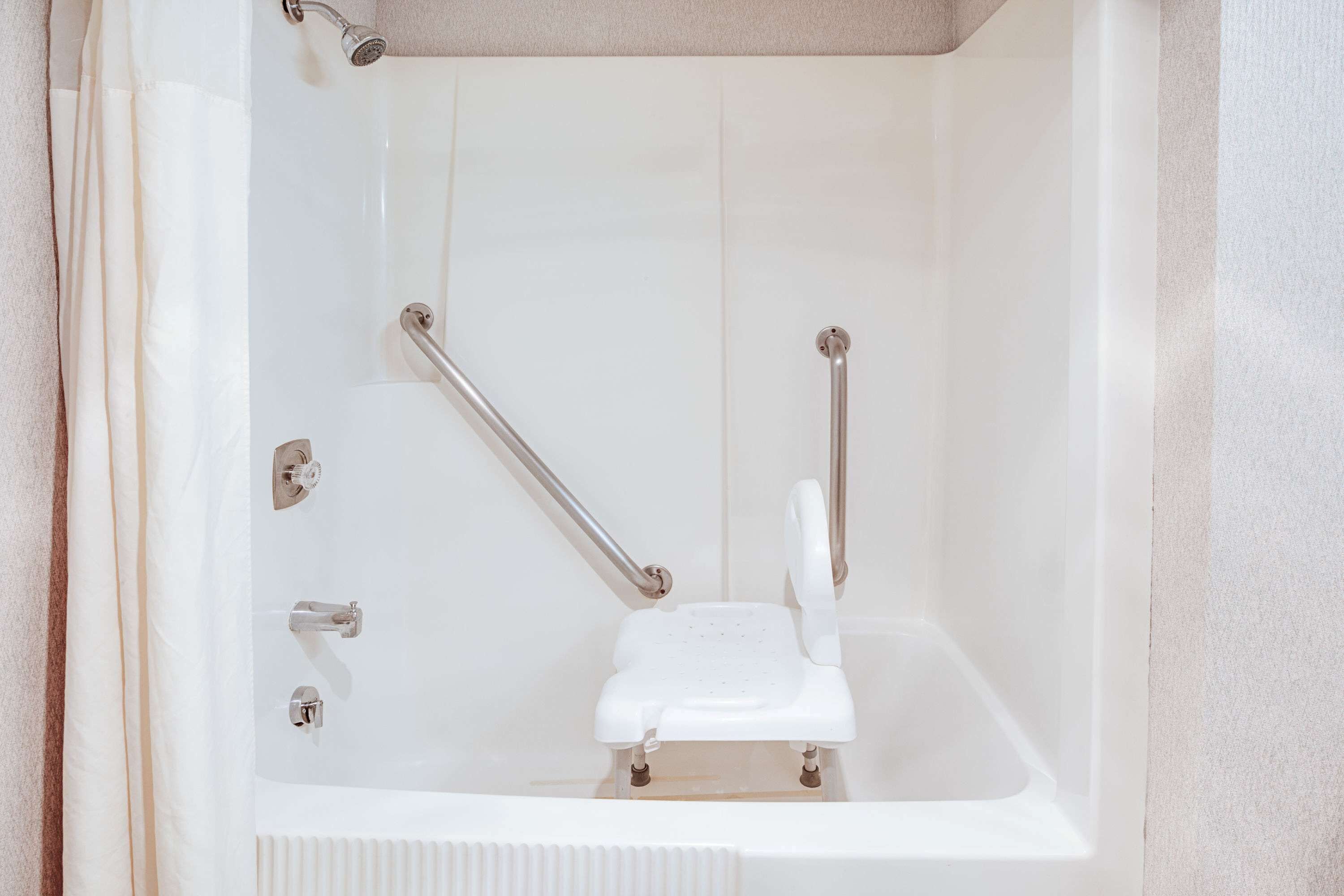Une baignoire blanche dotée d’un siège intégré et de barres d’appui.