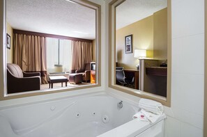 A hotel room with a large bathtub, a desk with a chair, and a view of the room's interior through a window.