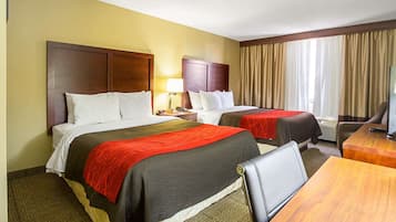 Quarto de hotel com duas camas, uma escrivaninha, uma cadeira, um abajur e uma janela com cortinas.
