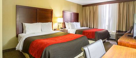 A hotel room with two beds, a desk, a chair, a lamp, and a window with curtains.