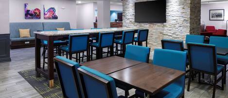 A modern lounge area with a bar, seating arrangements, and a flat-screen TV mounted on a stone wall.