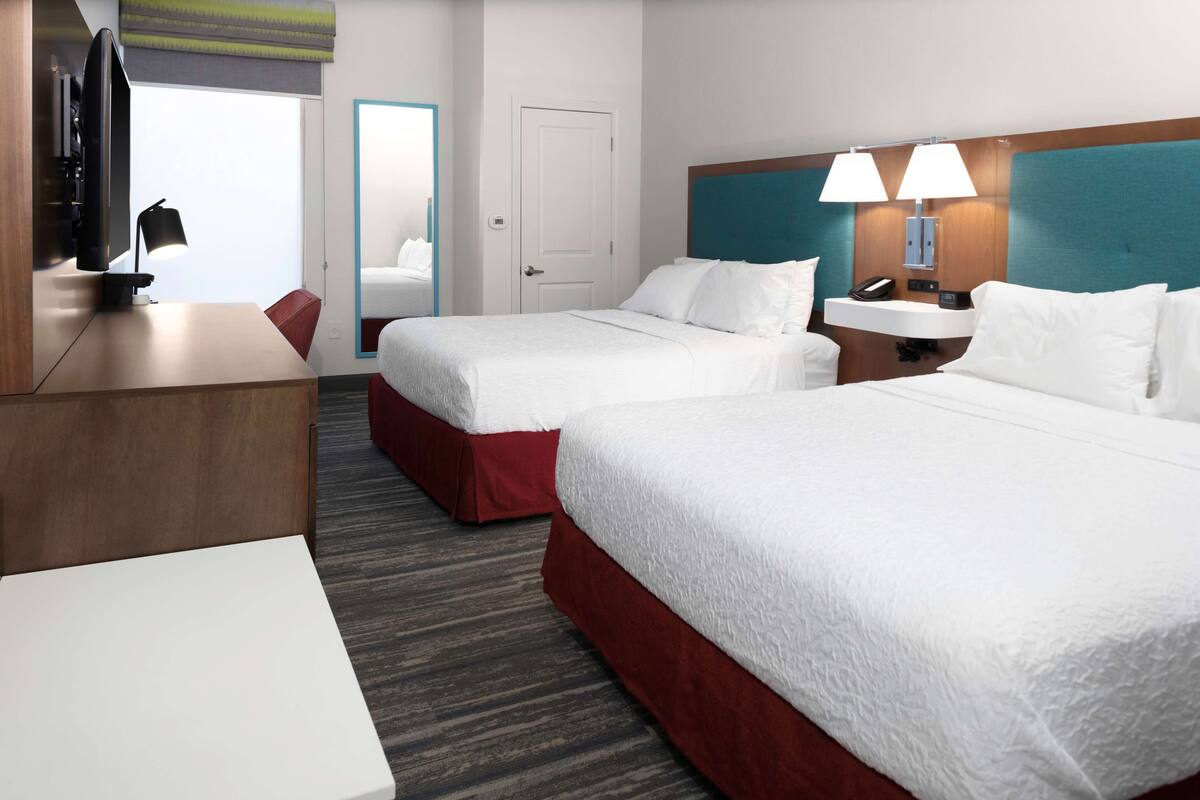 A hotel room with two beds, a desk, a TV, and a bathroom door.