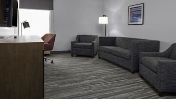 A modern office space with a desk, two armchairs, a sofa, a standing lamp, and a framed abstract painting on the wall.