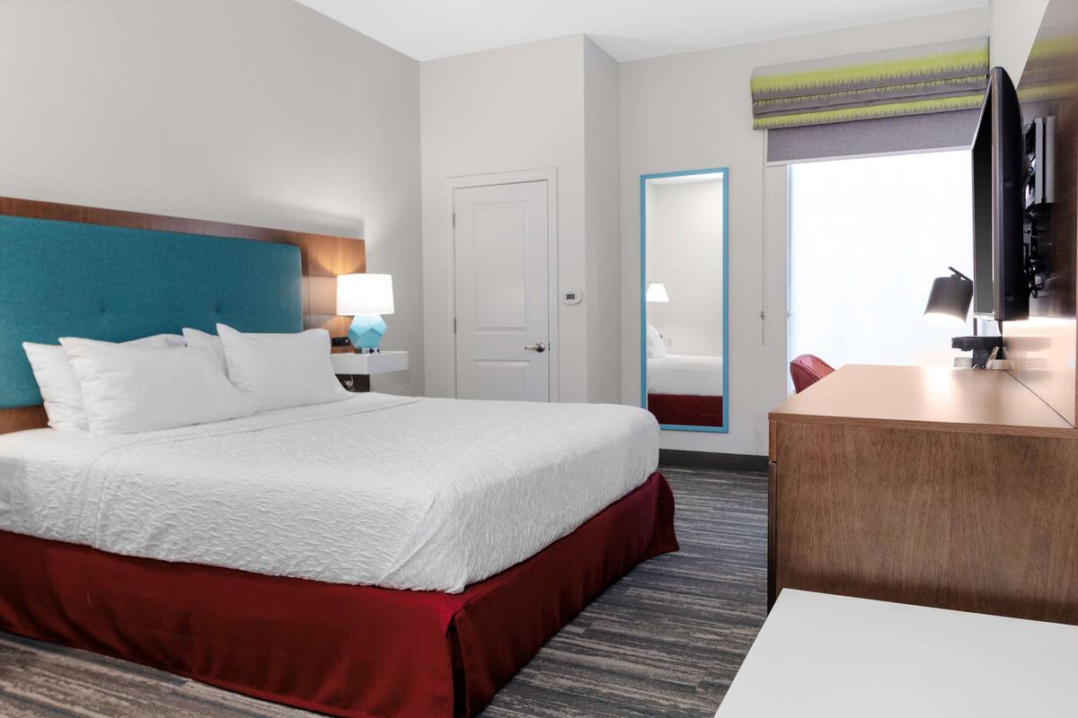 A hotel room with a large bed, a desk, a television, and a door leading to a bathroom.