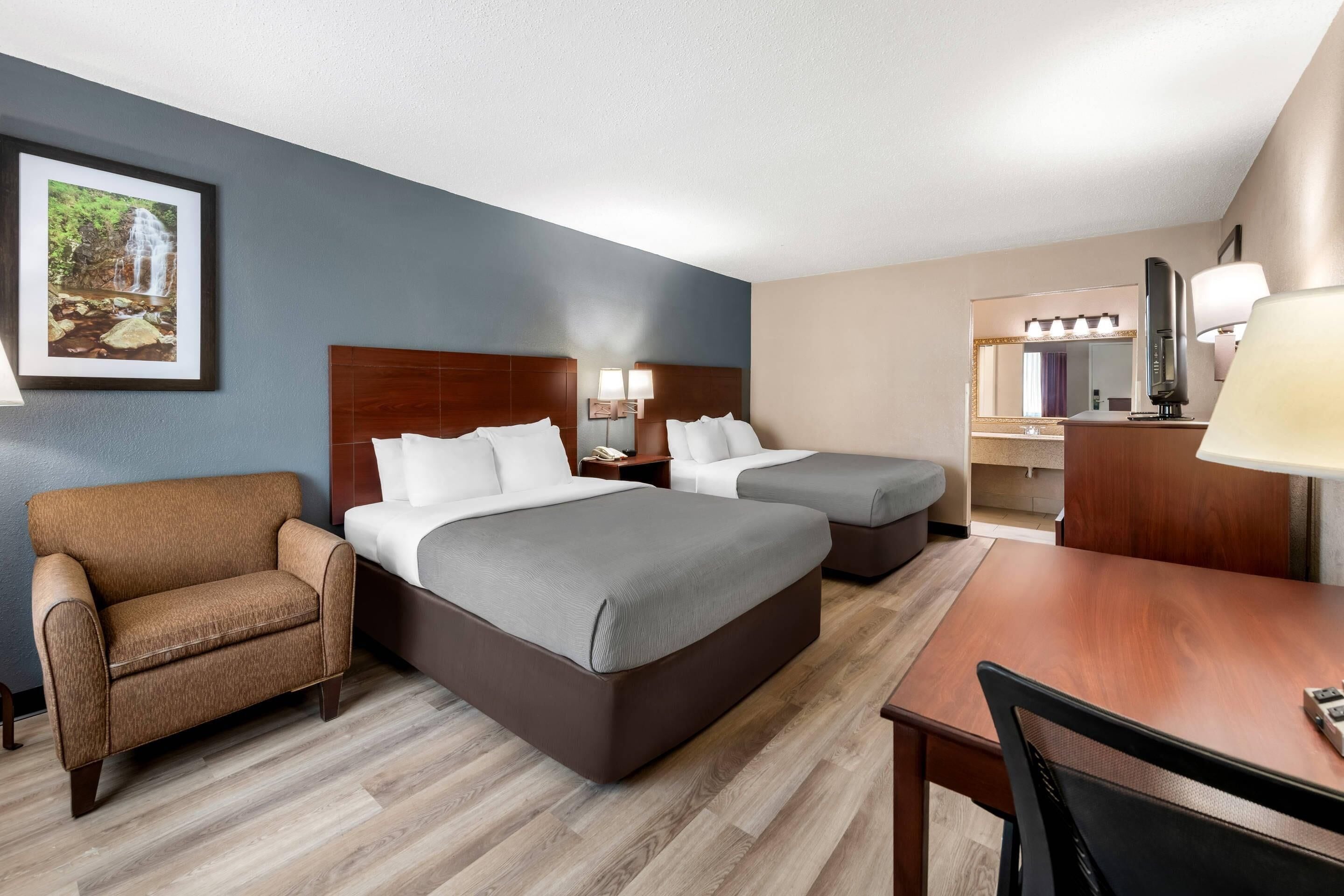Une chambre d’hôtel avec deux lits, un bureau, une chaise, une télévision et une salle de bain visible au fond.