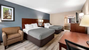 Une chambre d’hôtel avec deux lits, un bureau, une chaise, une télévision et une salle de bain visible au fond.