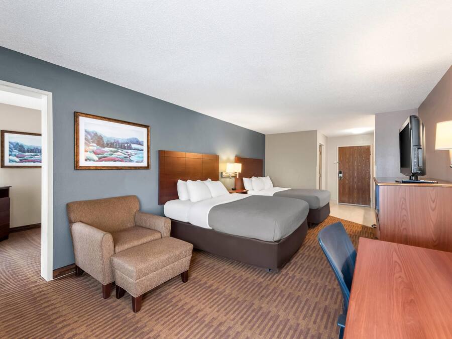 A hotel room with a bed, a chair, a desk, a television, and a lamp.