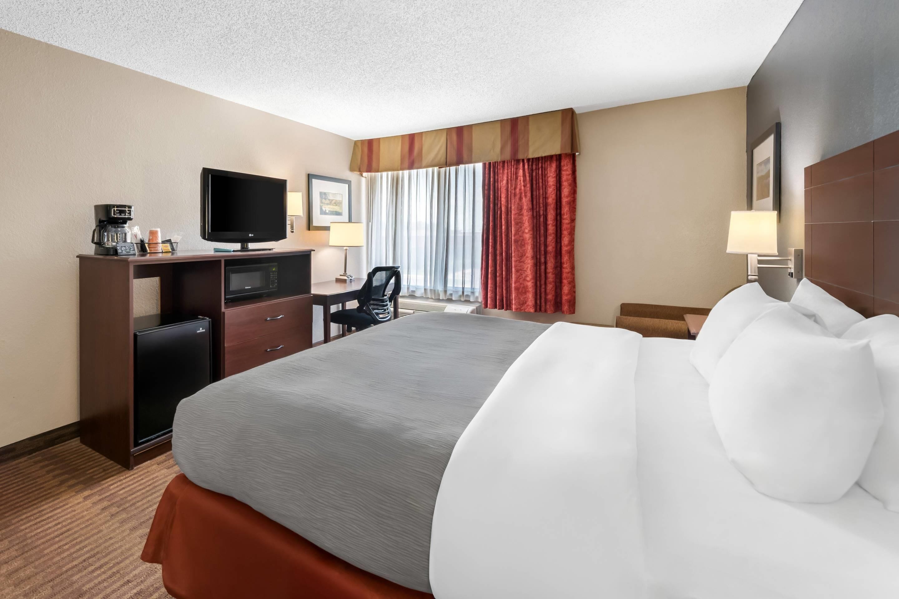 A hotel room with a bed, a desk with a television, a coffee maker, and a microwave.