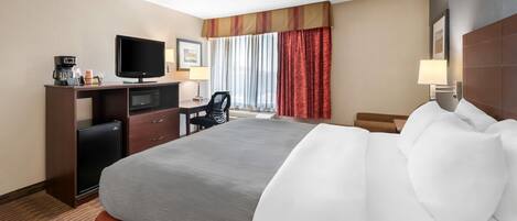 A hotel room with a bed, a desk with a television, a coffee maker, and a microwave.