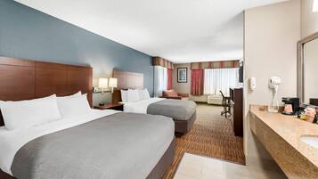 A hotel room with two beds, a desk, a chair, a bathroom, and a large mirror.