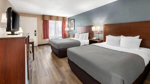 A hotel room with two beds, a desk, a television, and a window with curtains.
