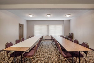 Un salón de conferencias con una larga mesa, sillas y dos ventanas con persianas.