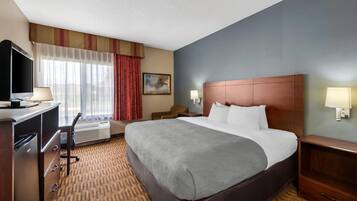 A hotel room with a large bed, a desk with a computer, a TV, a window with curtains, and a painting on the wall.