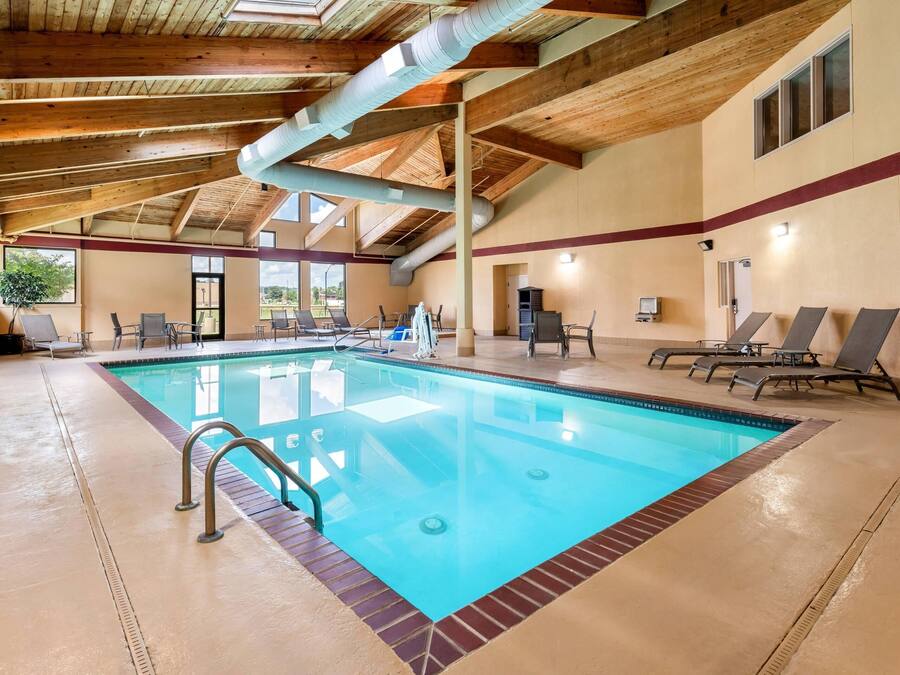 Una piscina interior con superficie de agua azul cristalina, rodeada de sillas de descanso y una estructura de techo de madera.