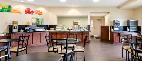 Un espacio para desayuno autoservicio con mesas, sillas y diversas opciones de comida.