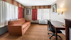 A hotel room with a sofa, a desk, an air conditioner, and a picture on the wall.