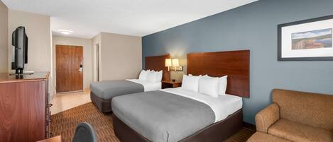 A hotel room with two beds, a desk, a chair, a television, and a framed picture on the wall.