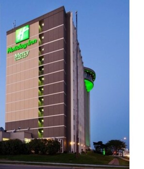 A Holiday Inn Express building with a prominent green 'HH' logo, a 'Mercy Campus' sign, and a curved green light feature on the side. - Holiday Inn Downtown - Mercy Area by IHG (Des Moines)