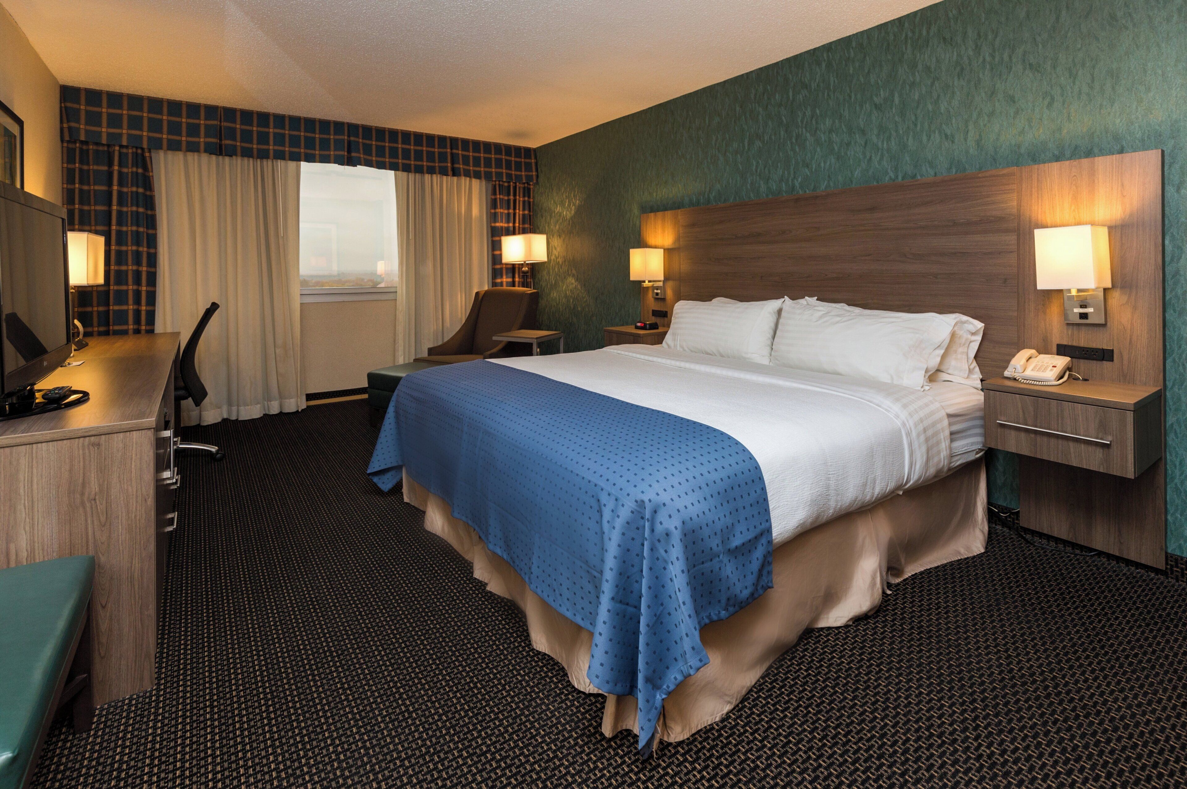 A hotel room with a bed, desk, chair, and a window with curtains.