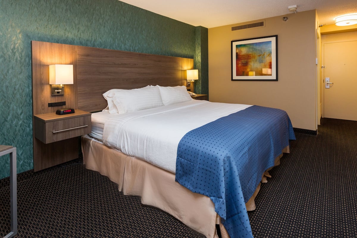 A hotel room with a large bed, two bedside tables with lamps, a wall-mounted painting, and a carpeted floor.