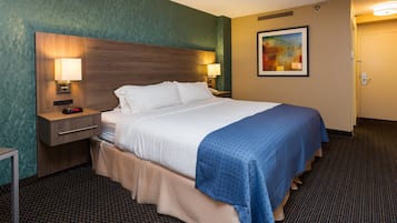 A hotel room with a large bed, two bedside tables with lamps, a wall-mounted painting, and a carpeted floor.