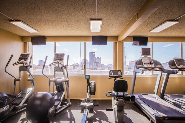 Ein Fitnessstudio mit verschiedenen Trainingsgeräten, großen Fenstern und Blick auf die Stadt.